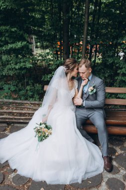 Güzel gelin ve damat parktaki ahşap bankta oturuyor.