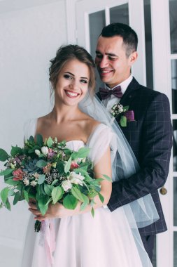 Güzel genç gelin ve yakışıklı damat düğün iç mekanında birlikte poz veriyorlar.            