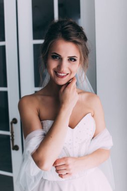 Beyaz elbiseli ve duvaklı güzel gelinin portresi düğün sabahı poz veriyor.            