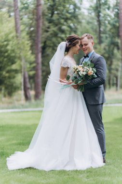 Güzel, mutlu bir düğün çifti parkta sarılıyor.   