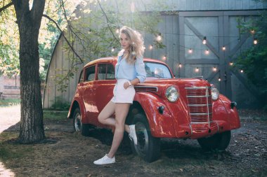 Kırmızı retro arabanın yanında poz veren güzel genç bir kadının portresi.         
