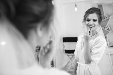 Mutlu genç gelin aynaya bakıyor ve makyaj yapıyor.