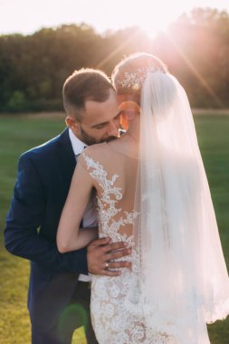 Mutlu gelin ve damat çifti güneş batarken yaz parkında poz veriyor.       