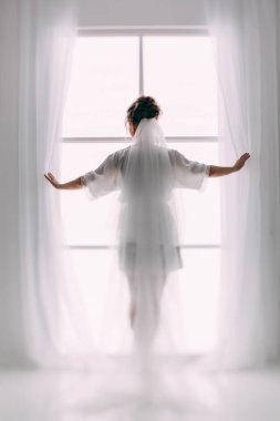 Pencere kenarında poz veren beyaz peçeli güzel gelinin arka manzarası          