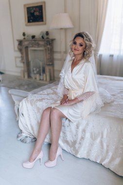 Yatakta oturmuş kameraya gülümseyen güzel sarışın gelin portresi.