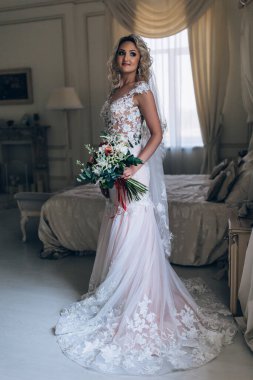 Beyaz elbiseli güzel sarışın gelin lüks içinde düğün buketi ile poz veriyor.              