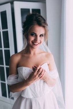 Beyaz elbiseli ve duvaklı güzel gelinin portresi düğün sabahı poz veriyor.            