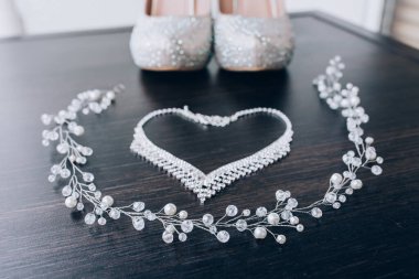 Koyu ahşap masa arkasında zarif düğün ayakkabıları ve mücevher manzarası.           