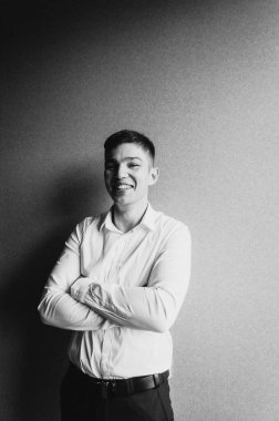 Beyaz gömlekli genç bir adamın portresi gri duvar arkasında poz veriyor.