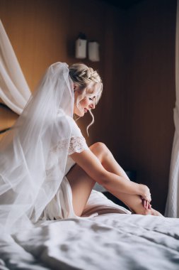 Genç, güzel sarışın gelin otel odasında yatakta poz veriyor.