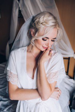 Genç, güzel sarışın gelin otel odasında yatakta poz veriyor.