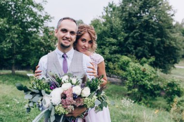 Güzel bir çift gelin ve damat doğada kucaklaşıyorlar.