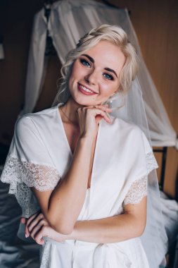 Genç, güzel sarışın gelin otel odasında yatakta poz veriyor.