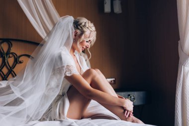 Genç, güzel sarışın gelin otel odasında yatakta poz veriyor.