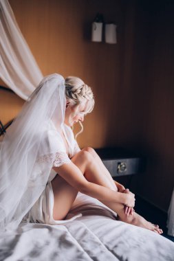 Genç, güzel sarışın gelin otel odasında yatakta poz veriyor.