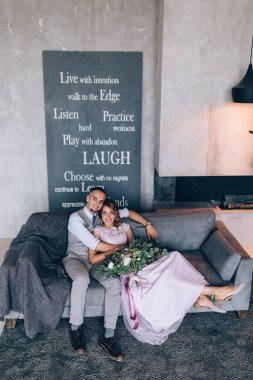 Kanepede poz veren genç ve güzel evliler ve arka planda cümleler var.