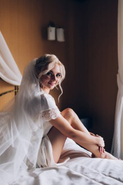 Genç, güzel sarışın gelin otel odasında yatakta poz veriyor.