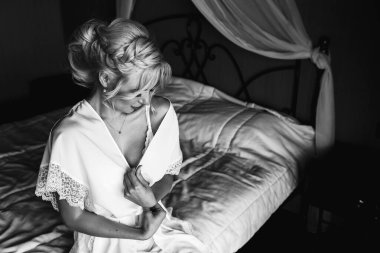 Genç ve güzel sarışın gelinin otel odasında yatakta poz verirken tek renkli fotoğrafı.