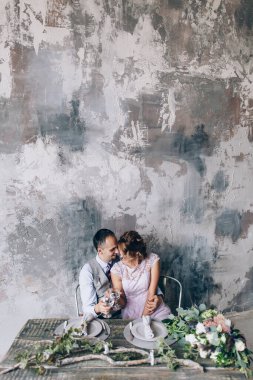 Genç ve mutlu bir çiftin portresi masada oturuyor ve bardaklarını tutuyor.                     