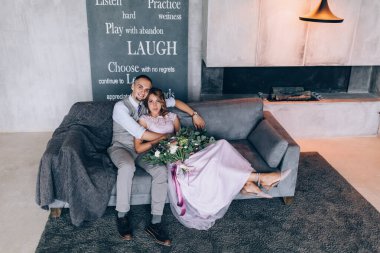 Kanepede poz veren genç ve güzel evliler ve arka planda cümleler var.