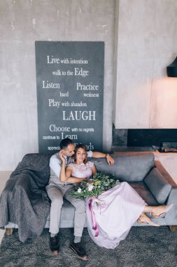 Kanepede poz veren genç ve güzel evliler ve arka planda cümleler var.