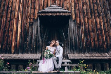 Güzel, mutlu gelin ve damat düğün günü eski ahşap kilisenin önünde oturuyor.        