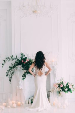 Gelinin arkadan görünüşü stüdyoda mumlarla süslenmiş zarifçe poz veriyor.