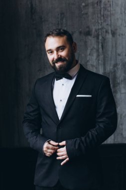 Siyah takım elbiseli yakışıklı bir adamın portresi. Arka planda papyon var.       