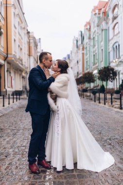 Güzel, mutlu genç gelin ve damat eski kasabanın arka planında öpüşüyorlar..