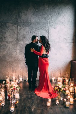 Siyah takım elbiseli zarif bir çift ve mumlarla aydınlatılmış kırmızı bir elbise.