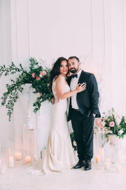 Güzel, mutlu, genç gelin ve damat düğün iç mekanında poz veriyor..       