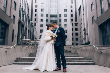 Güzel, mutlu genç gelin ve damat eski kasabanın arka planında öpüşüyorlar..