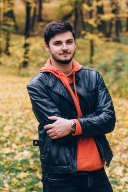 Sonbahar parkında kollarını kavuşturmuş genç bir adam. 