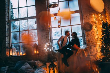 Genç bir çift, Noel süslemeleriyle dolu rahat bir stüdyoda poz veriyor. Yeni yılın aşk hikayesi..