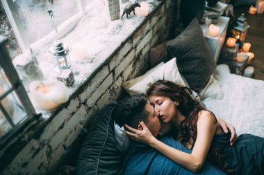 Yüksek açılı bir bakış açısıyla birbirine aşık genç çiftin rahat bir şekilde yatağında uzanması.          