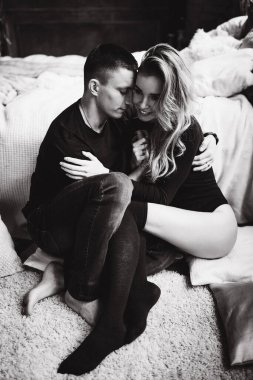 Sıcak bir odada, yatağın yanında oturan mutlu çift, siyah ve beyaz. 