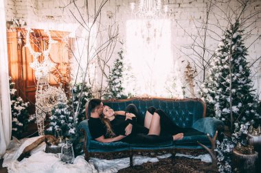 Genç ve güzel bir çift Noel ağacının yanındaki kanepede poz veriyor. 