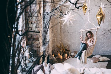 Sarışın bir kadın, rahat bir stüdyoda salıncakta sallanıyor, huzurlu atmosferin tadını çıkarıyor. 