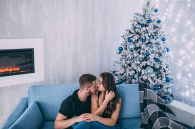 Genç bir çift, Noel süslemeleriyle dolu rahat bir stüdyoda poz veriyor. Yeni yılın aşk hikayesi..