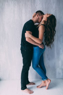 Genç ve mutlu çift, gri duvarda sarılıp öpüşüyorlar.
