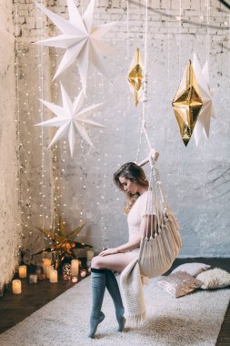 Sarışın bir kadın, rahat bir stüdyoda salıncakta sallanıyor, huzurlu atmosferin tadını çıkarıyor. 