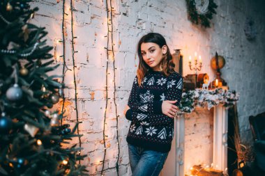 Kışın süveter giyen genç bir kadın Noel süslerinin yanında poz veriyor. 