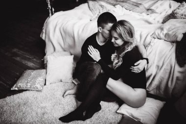 Sıcak bir odada, yatağın yanında oturan mutlu çift, siyah ve beyaz. 