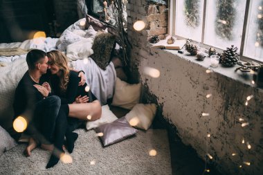 Mutlu çift, Noel süslemeleri olan rahat bir odada, yatağın yanında oturuyor.