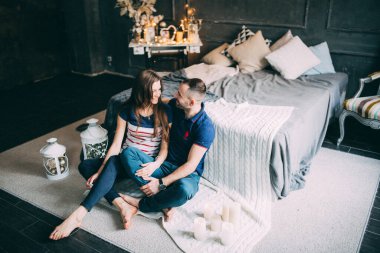 Genç aşık çift dekore edilmiş stüdyoda yatağın yanında oturuyor. 