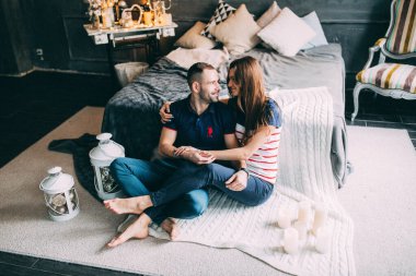 Genç aşık çift dekore edilmiş stüdyoda yatağın yanında oturuyor. 