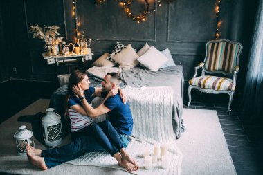 Genç aşık çift dekore edilmiş stüdyoda yatağın yanında oturuyor. 