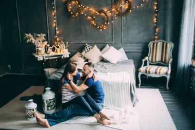 Genç aşık çift dekore edilmiş stüdyoda yatağın yanında oturuyor. 