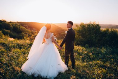 Gelin ve damat çifti düğün günlerinde gün batımında doğada yürüyorlar.         