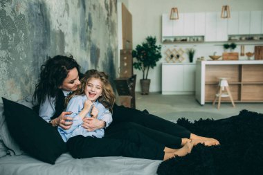 Stüdyo odasında yatakta poz veren genç mutlu anne ve kız. 